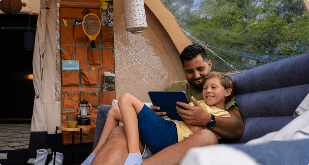 vader en zoon op opblaasbare bank Vader en zoon ontspannen samen op een opblaasbare bank in een luxe tent, kijkend naar een tablet terwijl ze genieten van hun glamping ervaring