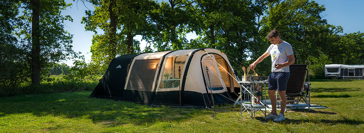 basic, pro, premium tenten op campingveldje met man die aan het koken is